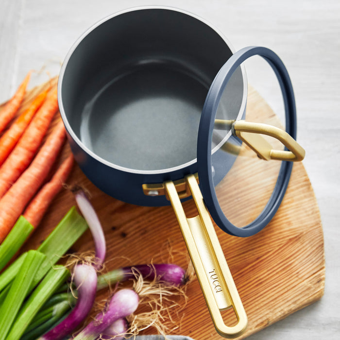 Blue 2-quart saucepan with lid on a board, next to carrots, green onions, and celery.