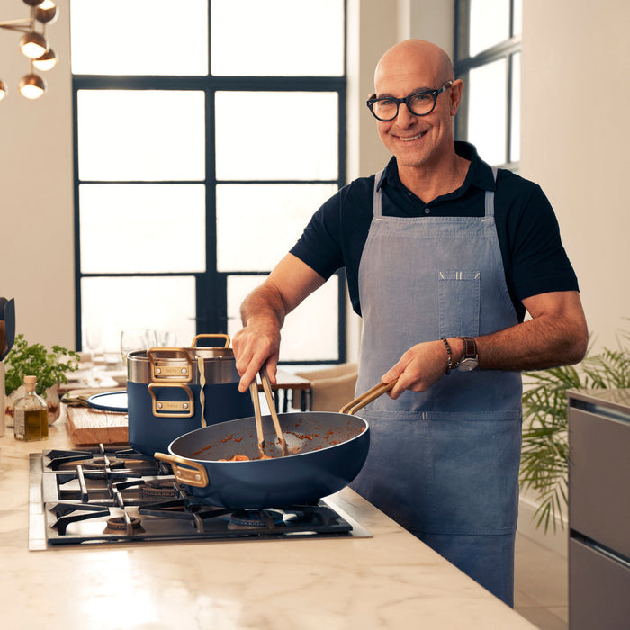 Man in glasses and apron cooking with a blue Stanley Tucci 4-quart saucepan in a modern kitchen.