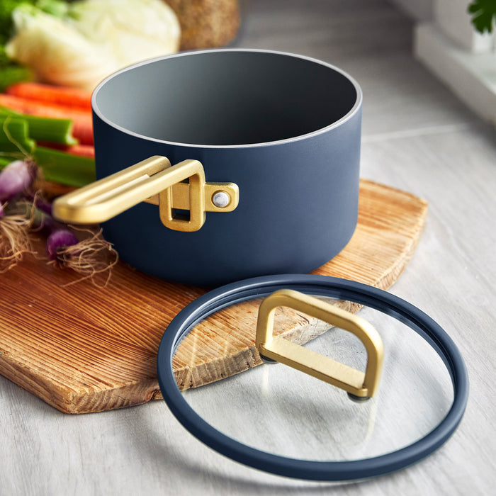 Marino blue ceramic nonstick saucepan with lid on a wooden board next to fresh vegetables.