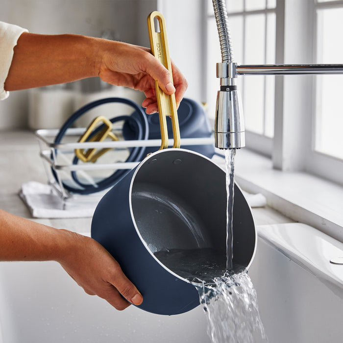 Ceramic nonstick blue saucepan being rinsed at a kitchen sink.