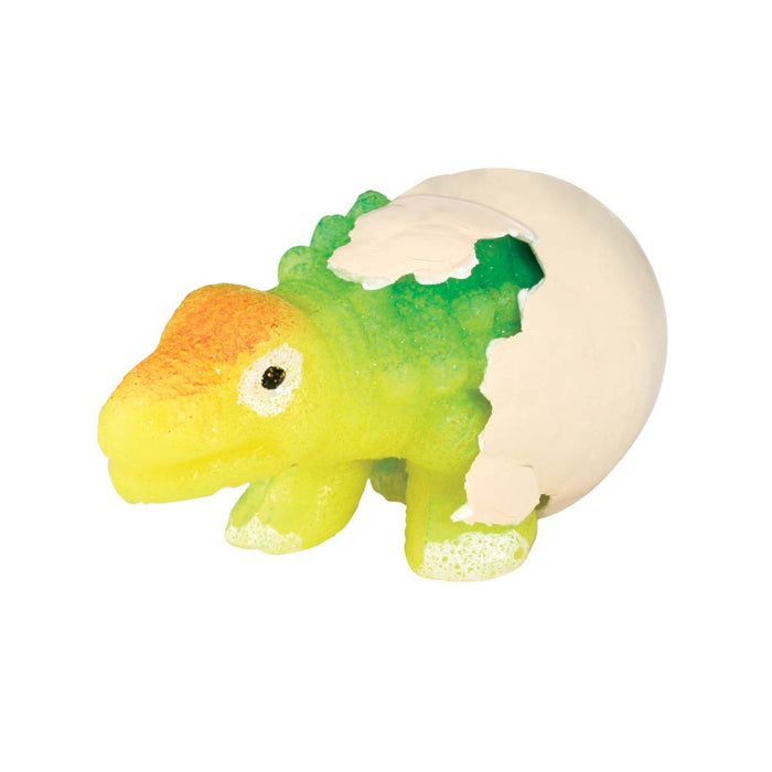 A Toysmith Hatchin' Grow Dino, a small, colorful expanding dinosaur toy, is partially emerging from a cracked white eggshell. Its green, yellow, and orange body stands out against the plain white background.