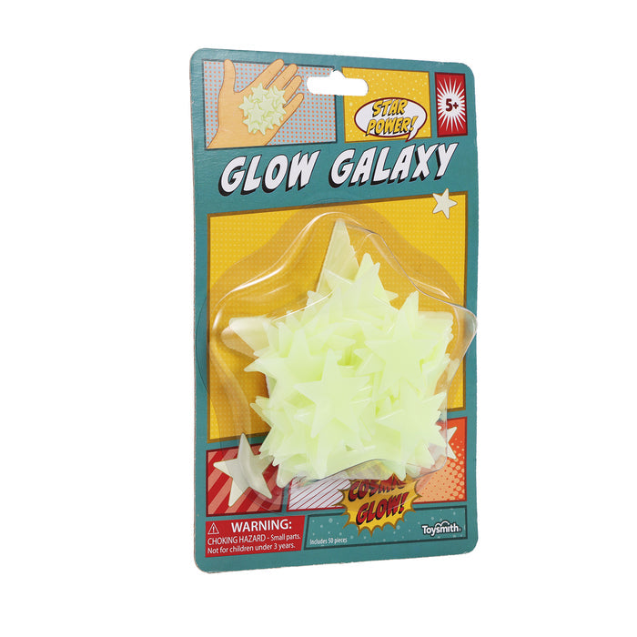 A space-inspired package labeled YAY! Glow Galaxy from the brand Comic Book contains glow-in-the-dark star shapes. The packaging displays hands holding stars, includes a choking hazard warning, and presents the stars arranged in a plastic bubble.