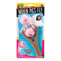 The YAY! When Pigs Fly toy by YAY! features two pink flying pig balls and a brown tree-shaped slingshot in humorous packaging with “Fling Em!” and “How high can they go?” plus a warning label at the bottom.